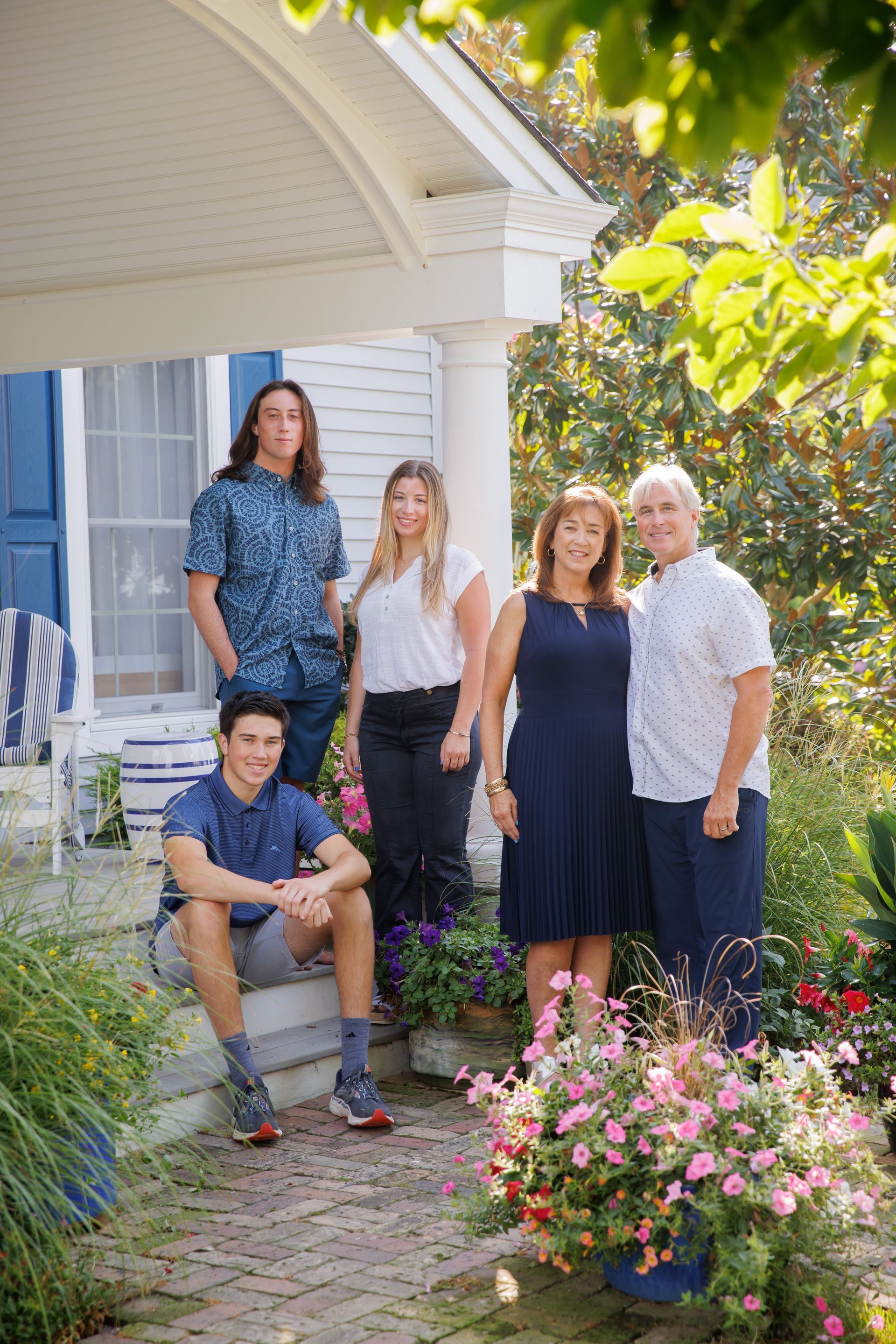 Five people posing beside a house and flower garden on a sunny day