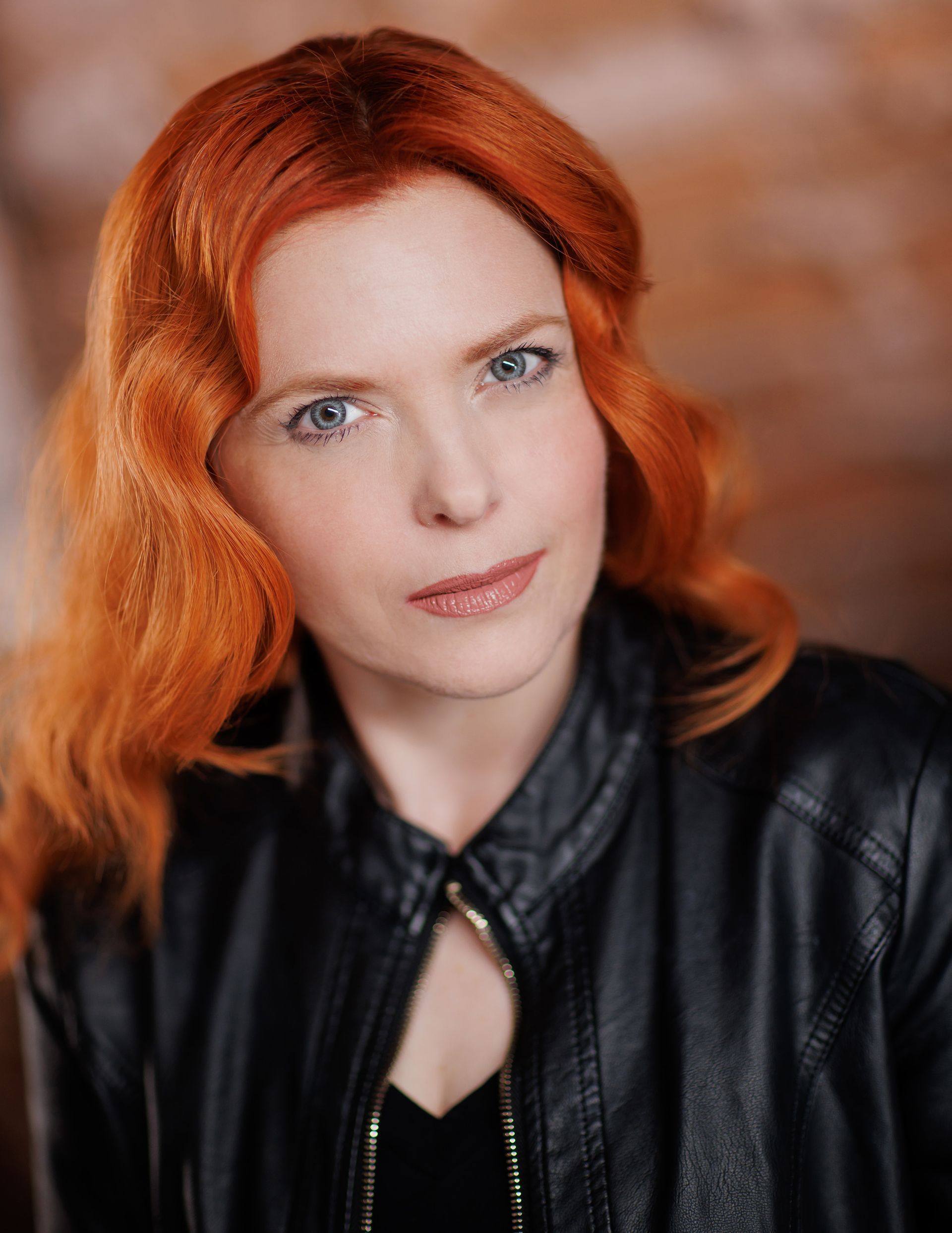 Portrait of a person with bright red hair in a black jacket against a warm blurred background
