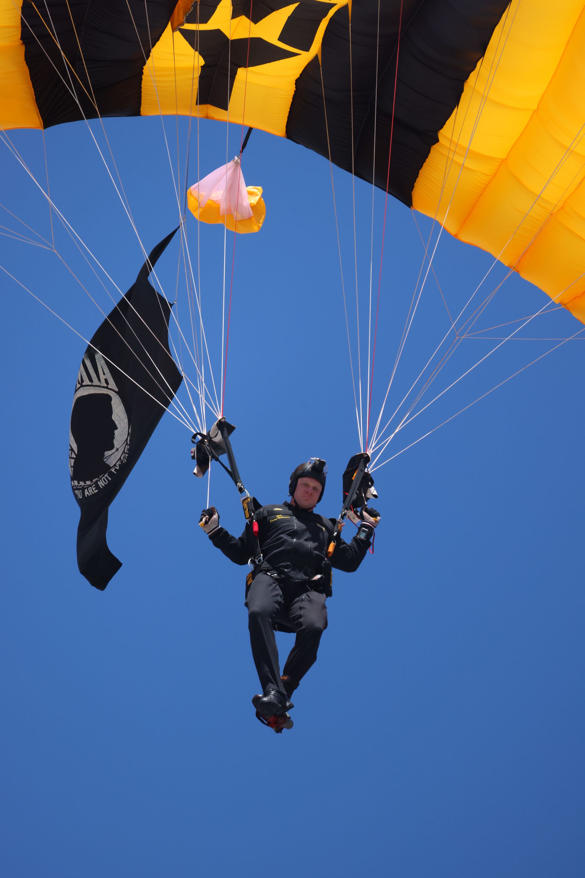 Skydiver dangling beneath a yellow parachute against a clear blue sky