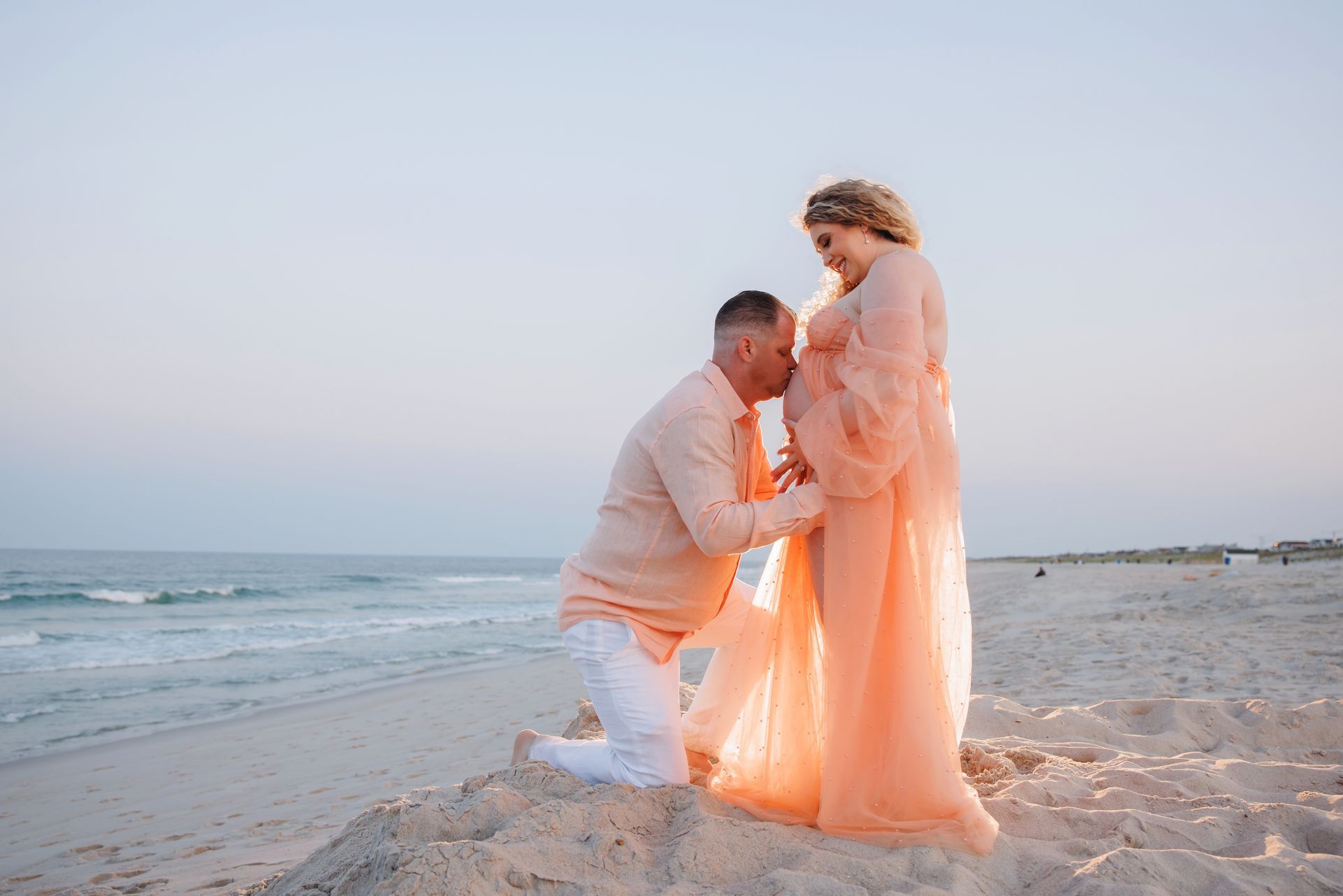 Couple in peach attire embracing on a sandy beach at sunset