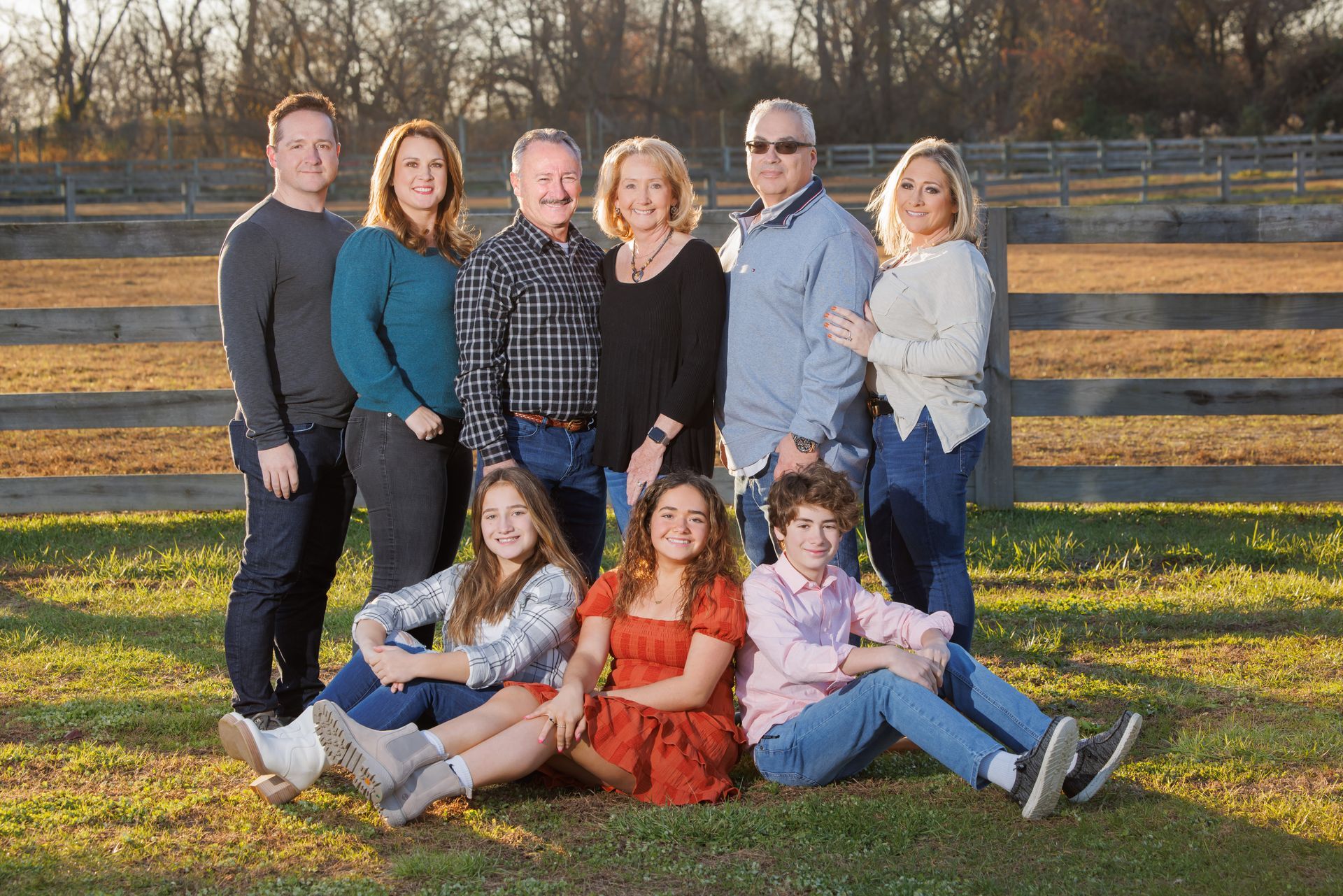 Group portrait of seven people posing outdoors by a wooden fence in warm evening light