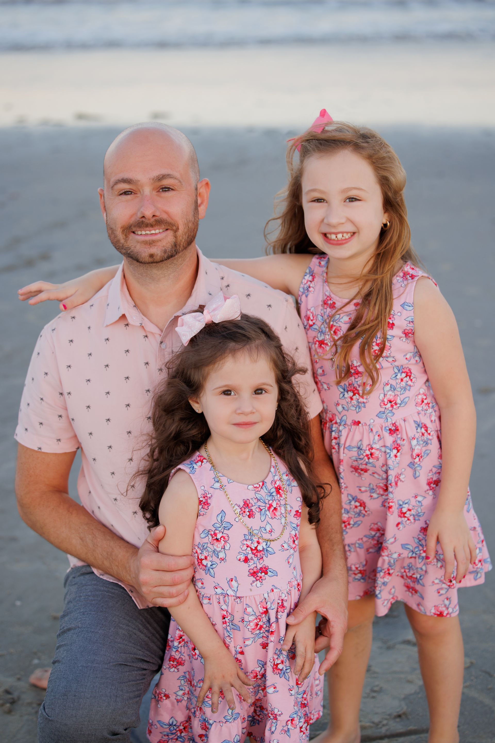 Three people in matching floral outfits smiling on a beach at sunset