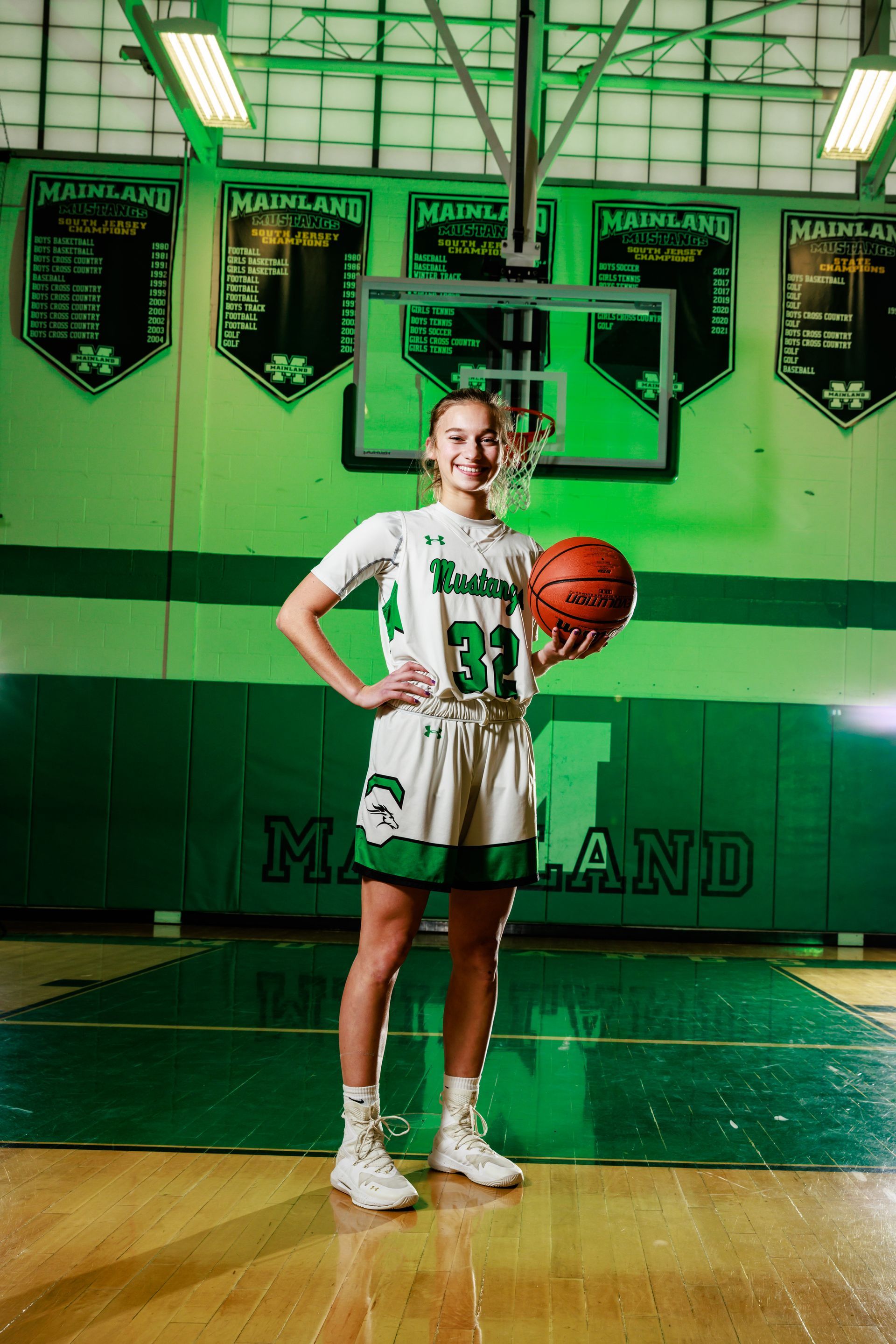 Basketball player in white uniform holding a ball on a gym court with green banners in the background