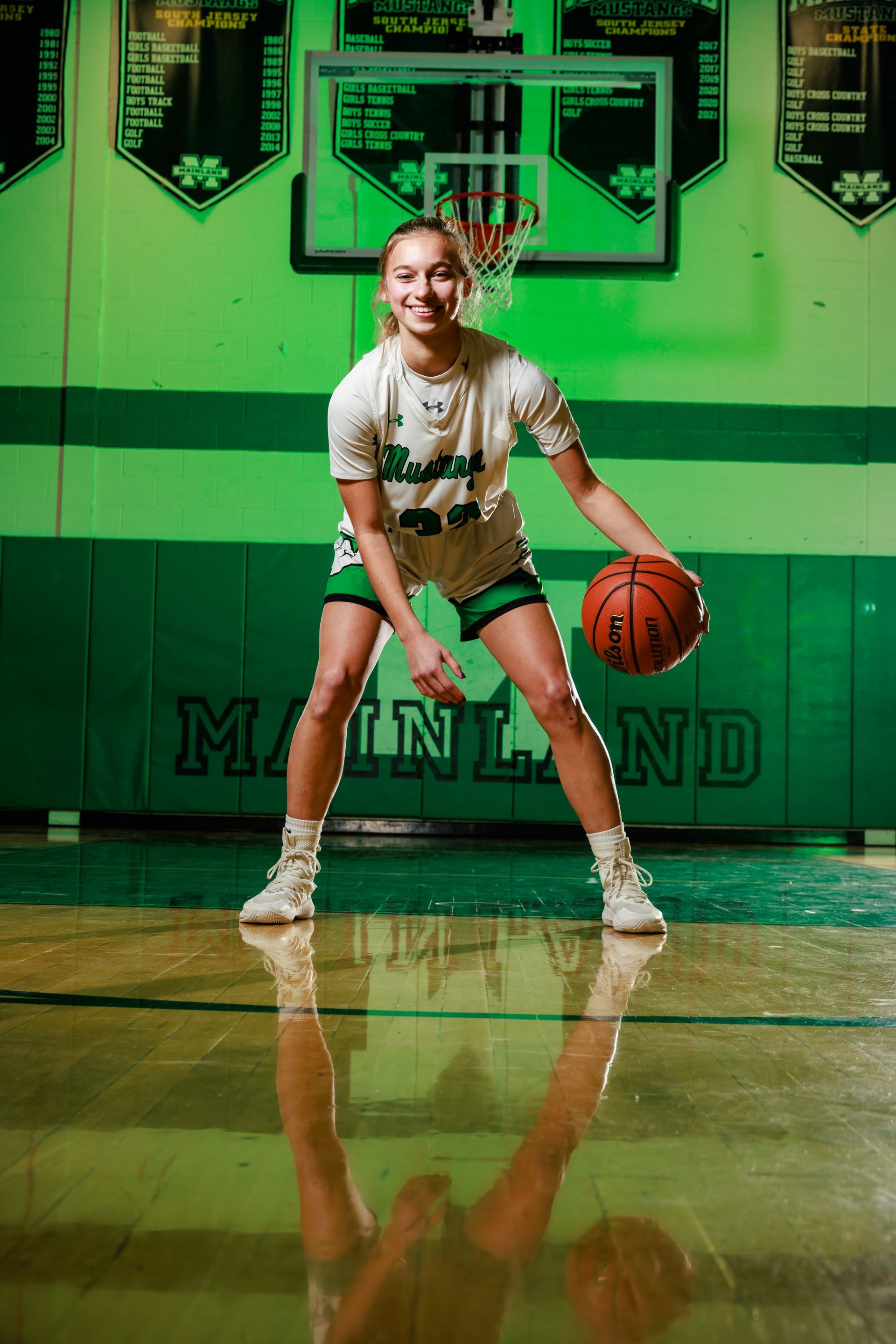 Basketball player dribbling on a green court in a gym with hoop and backboard
