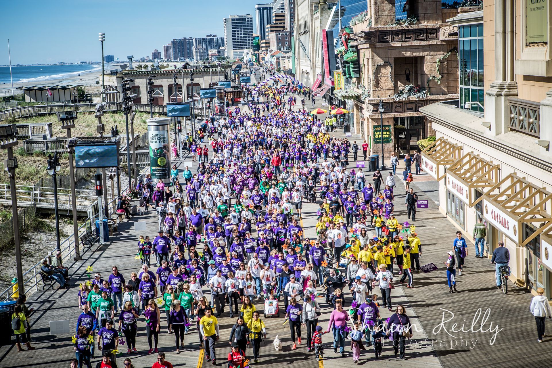 Large crowd of runners in colorful shirts racing down a seaside city street
