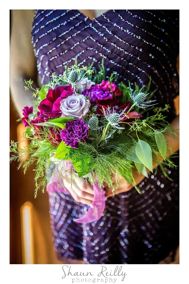 Bouquet of purple, pink, and green flowers held against a dark sequined dress