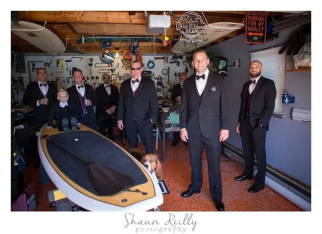 Men in suits gathered around a small boat in a cluttered garage workspace
