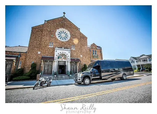 Brick church facade with circular window, a black van parked outside, and a bicycle on the street under a blue sky