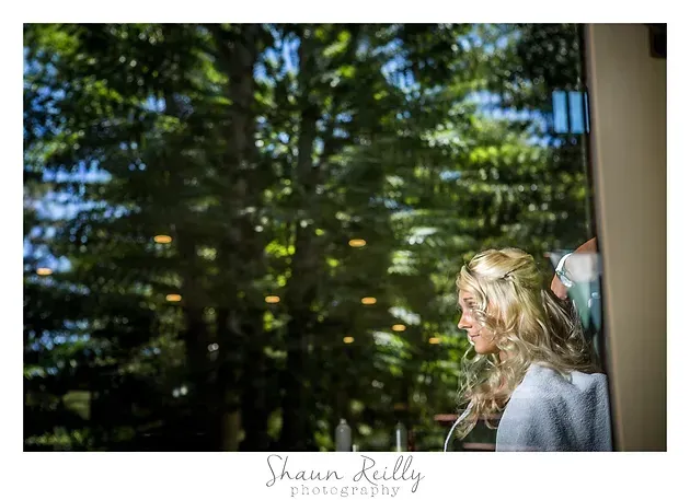Blonde person looking out a window at trees and sunlight outdoors