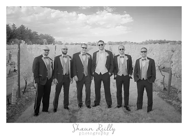Six men in suits stand in a vineyard under a cloudy sky, posing for a formal black-and-white portrait.