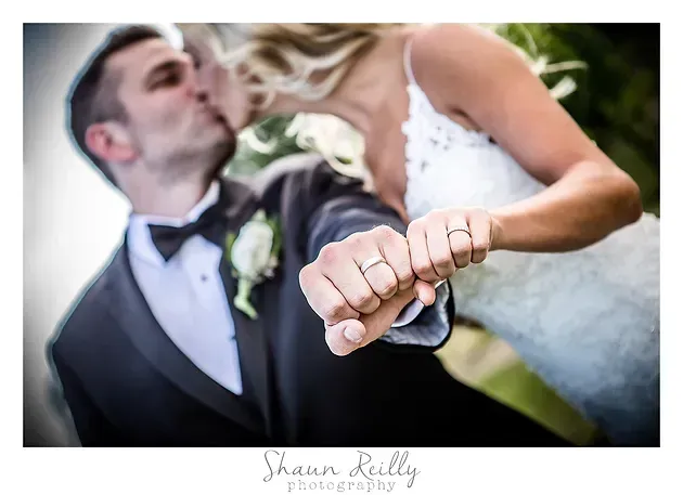 Wedding couple kissing, bride’s hand with ring held in the foreground