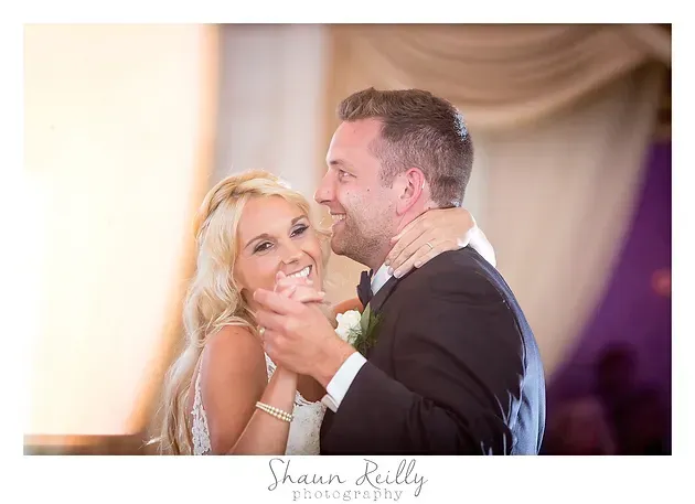 Couple dancing closely at a wedding reception, smiling in a softly lit indoor venue