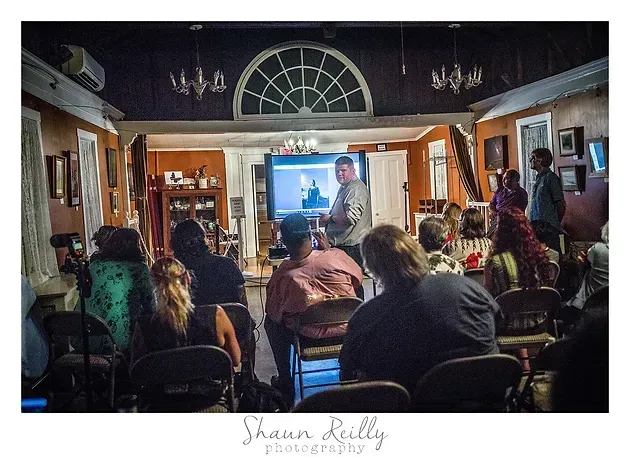 Audience seated in a room watching a speaker on a large screen at the front