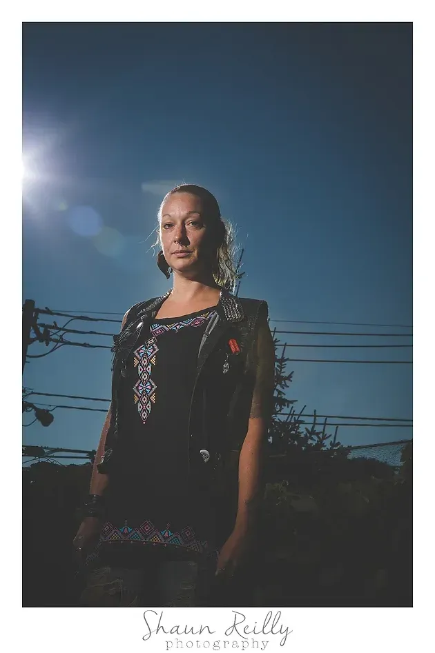 Portrait of a woman in a black dress standing outdoors at dusk, with a bright lens flare and power lines behind her