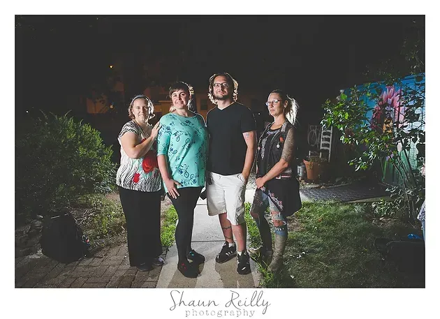 Four friends posing outdoors at night, lit by colorful lights.