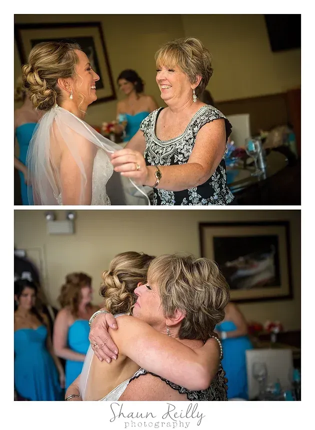 Two women embracing and smiling at a wedding reception, with guests blurred in the background