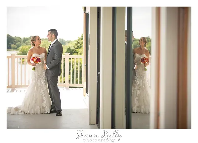 Bride and groom sharing a quiet moment on a bright balcony, reflected in a nearby mirror.
