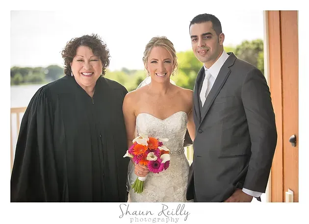 Bride holding a colorful bouquet with two attendants, standing in a doorway and smiling
