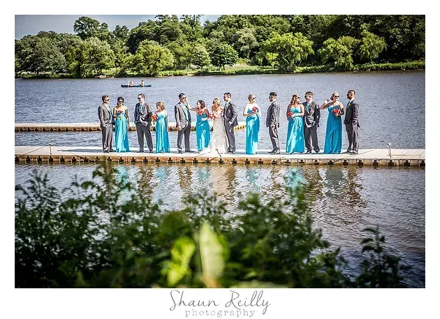 Wedding party in blue dresses and gray suits posing on a dock by a lake