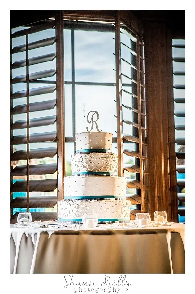 Three-tier wedding cake on table by sunlit window with wooden shutters