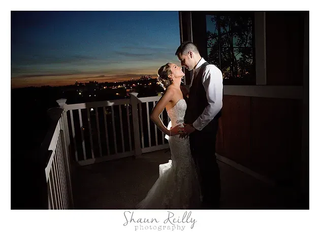 Bride and groom embracing on a balcony at sunset with city lights in the background