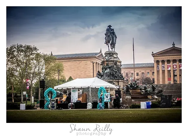 Outdoor market tent in a city square beneath a large statue and historic buildings
