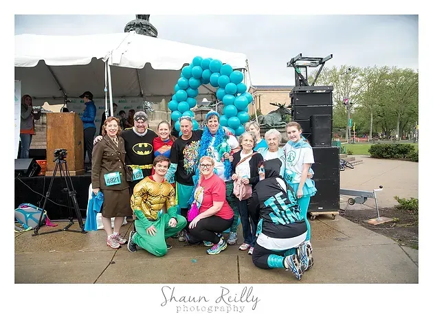 Group posing outdoors under a blue balloon arch at a community event