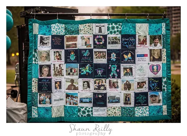 Quilt with many small photo squares, teal and white border, displayed on a wall.