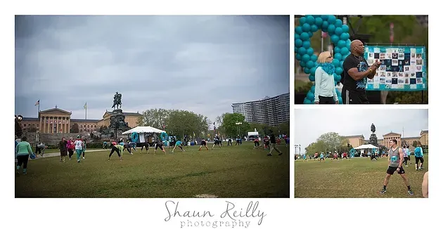 Outdoor fair with a large turquoise balloon sculpture and people gathered on a grassy field under a cloudy sky