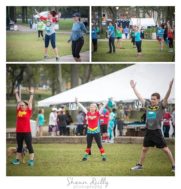 Runners doing jumping jacks in a park during a group fitness event, with spectators nearby.