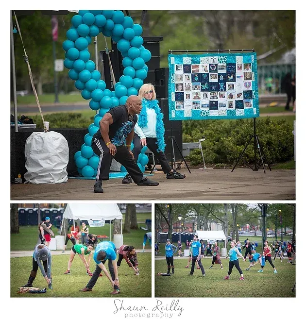 Outdoor fitness event with people exercising on a grassy field beside a turquoise balloon heart and photo display