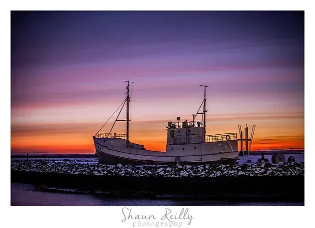Fishing boat at sunset on a rocky shore, silhouetted against a purple and orange sky
