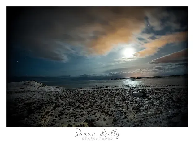 Cloudy beach at dusk with a bright sun reflecting on calm water