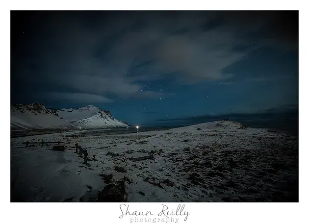 Snowy mountain coast under a dark cloudy sky with a faint light on the horizon.
