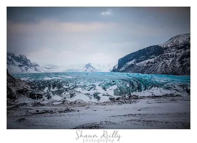 Snowy mountains and a turquoise glacier under a cloudy winter sky