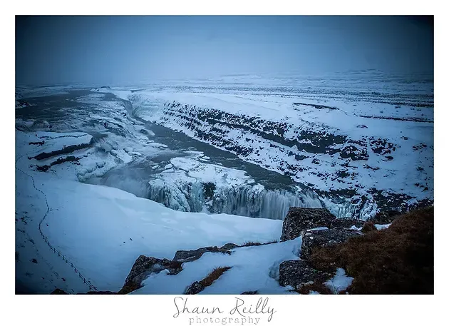 Snow-covered canyon with a frozen waterfall and icy river under a blue winter sky