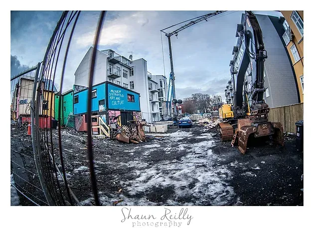 Construction site with excavators beside a blue building on a snowy, muddy street