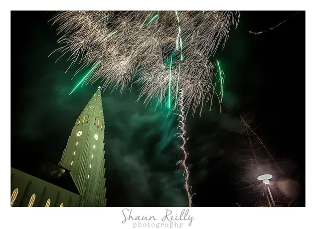 Fireworks bursting above a lit pointed tower at night