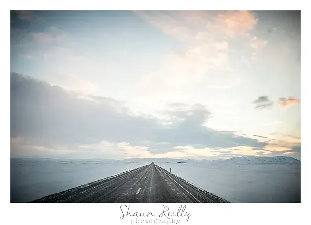 Long wooden pier leading into a calm ocean under a soft pastel sunrise sky
