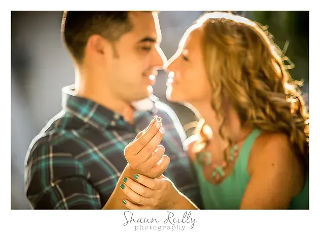 Couple facing each other outdoors, smiling and holding hands in warm sunlight