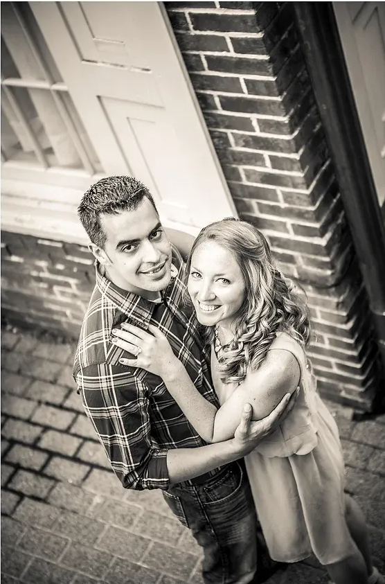 Couple embracing on a brick porch, smiling up at the camera near a front door