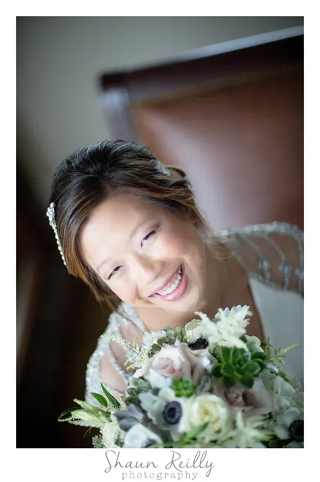 Smiling woman holding a white and green bouquet in a softly lit portrait