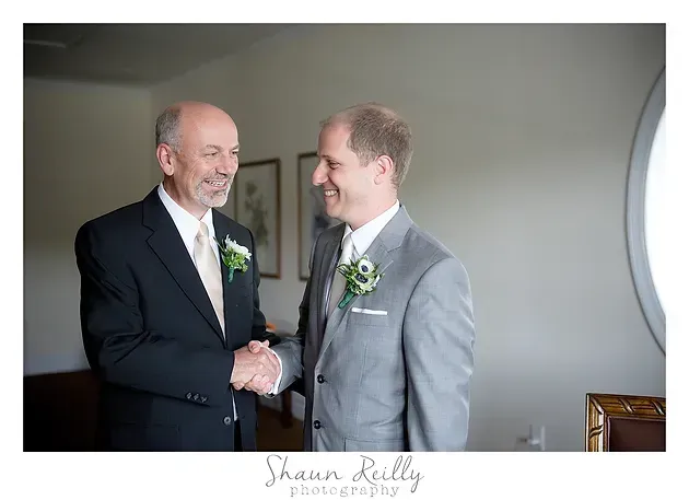 Two men in suits smiling and shaking hands indoors at a formal event