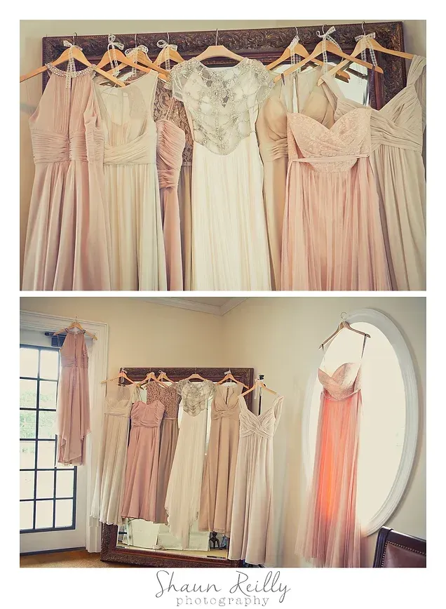 Pastel wedding dresses hanging on a rack in a boutique, with a peach gown displayed by a window