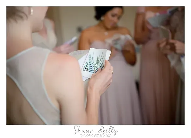 Woman holding a card reading a note while bridesmaids in lavender dresses get ready nearby