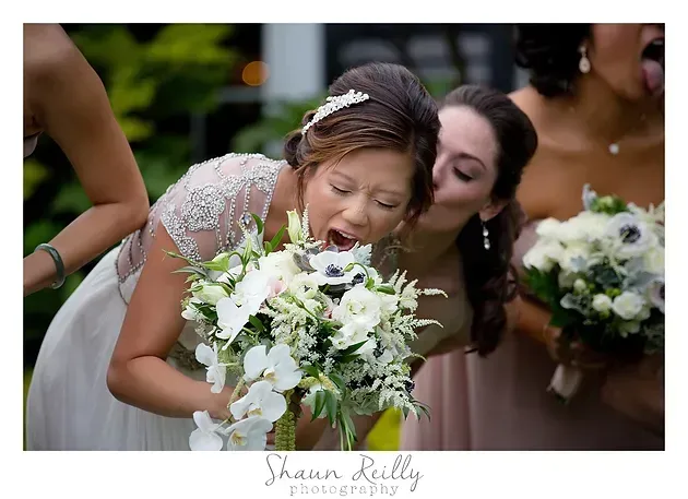 Bride laughing as she leans toward a white bouquet at an outdoor wedding