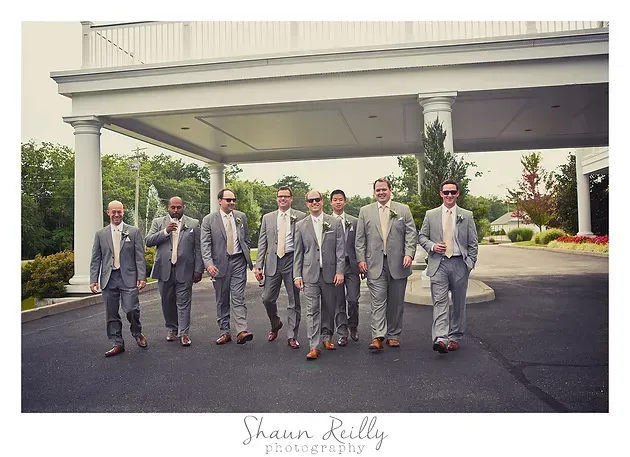 Six men in gray suits and sunglasses walking outside a building with covered entrance