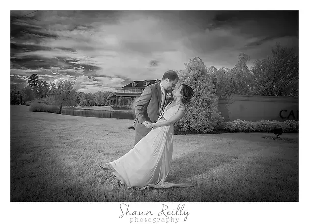 Black-and-white wedding couple dancing outdoors, bride’s dress flowing in the wind