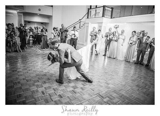 Wedding couple dancing on a parquet floor, surrounded by guests in a bright reception hall