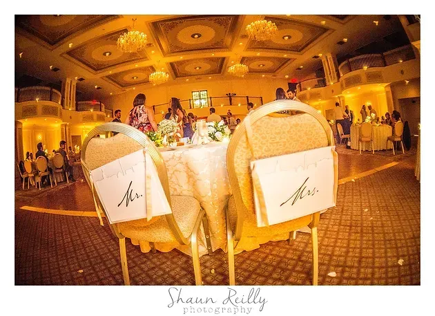 Decorated wedding reception table with chairs in a warm-lit ballroom